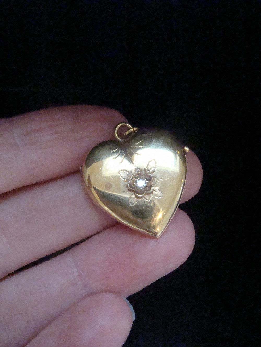 An antique gold heart-shaped locket featuring floral hand engraving and a central flush-set diamond.
