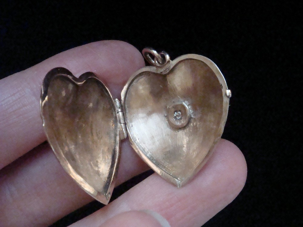 An Edwardian 9ct gold puffed heart locket featuring a centrally inset old cut diamond within a starburst setting. View V