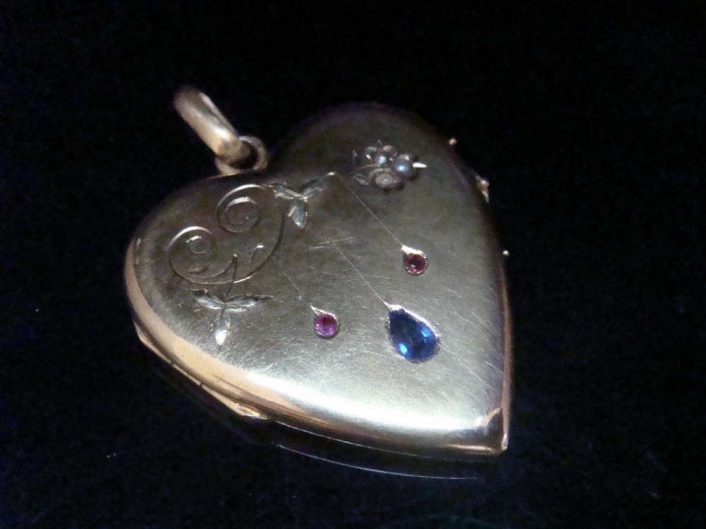 A heart-shaped 18ct yellow gold locket decorated with botanical engravings, a central pear-cut blue sapphire, two small rubies, and seed pearls. View II