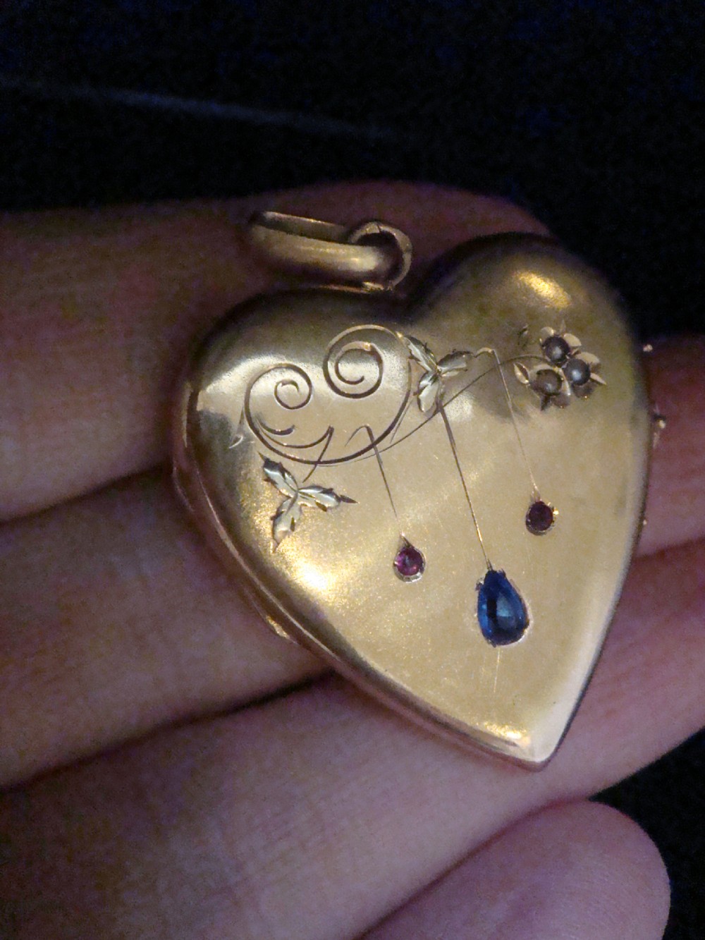 A heart-shaped 18ct yellow gold locket decorated with botanical engravings, a central pear-cut blue sapphire, two small rubies, and seed pearls. View III