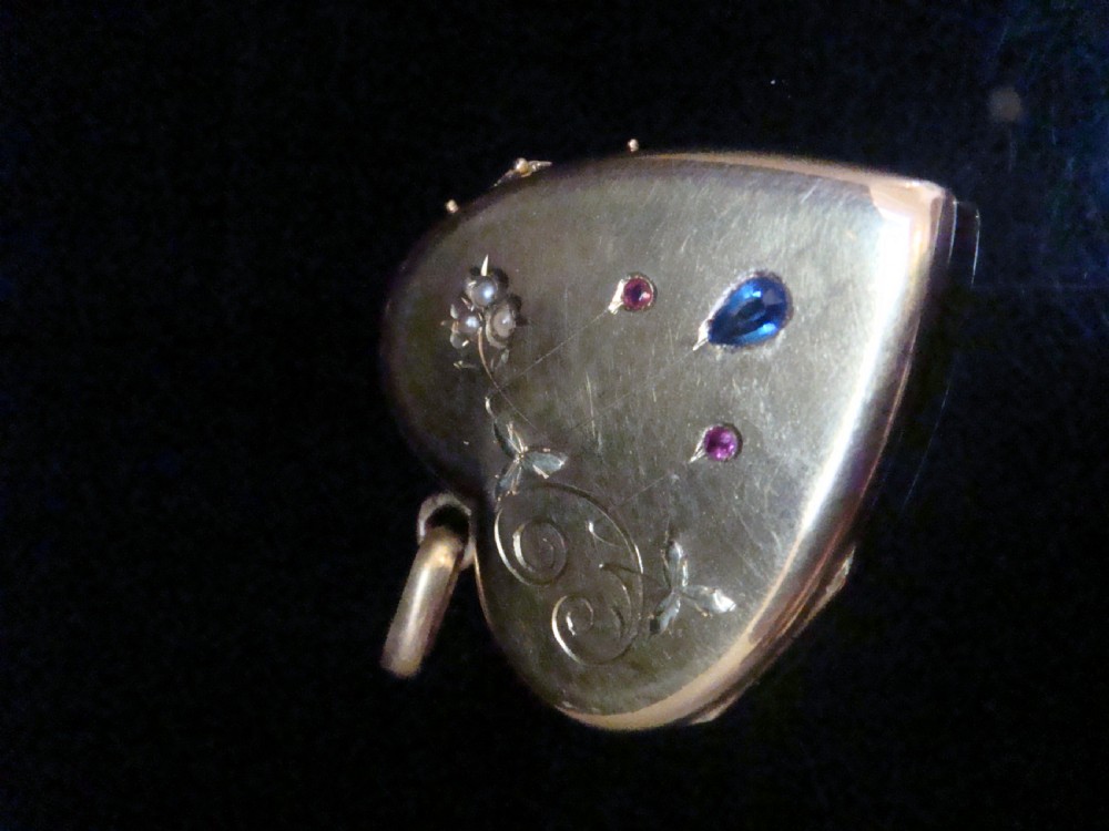 A heart-shaped 18ct yellow gold locket decorated with botanical engravings, a central pear-cut blue sapphire, two small rubies, and seed pearls. View IV