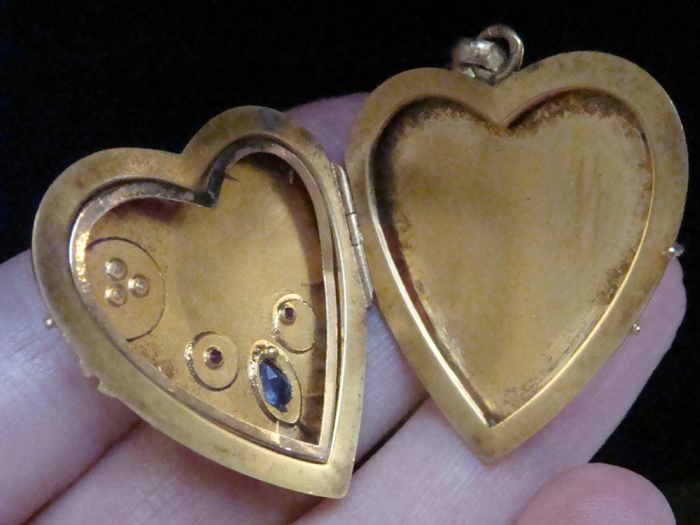 A heart-shaped 18ct yellow gold locket decorated with botanical engravings, a central pear-cut blue sapphire, two small rubies, and seed pearls. View V