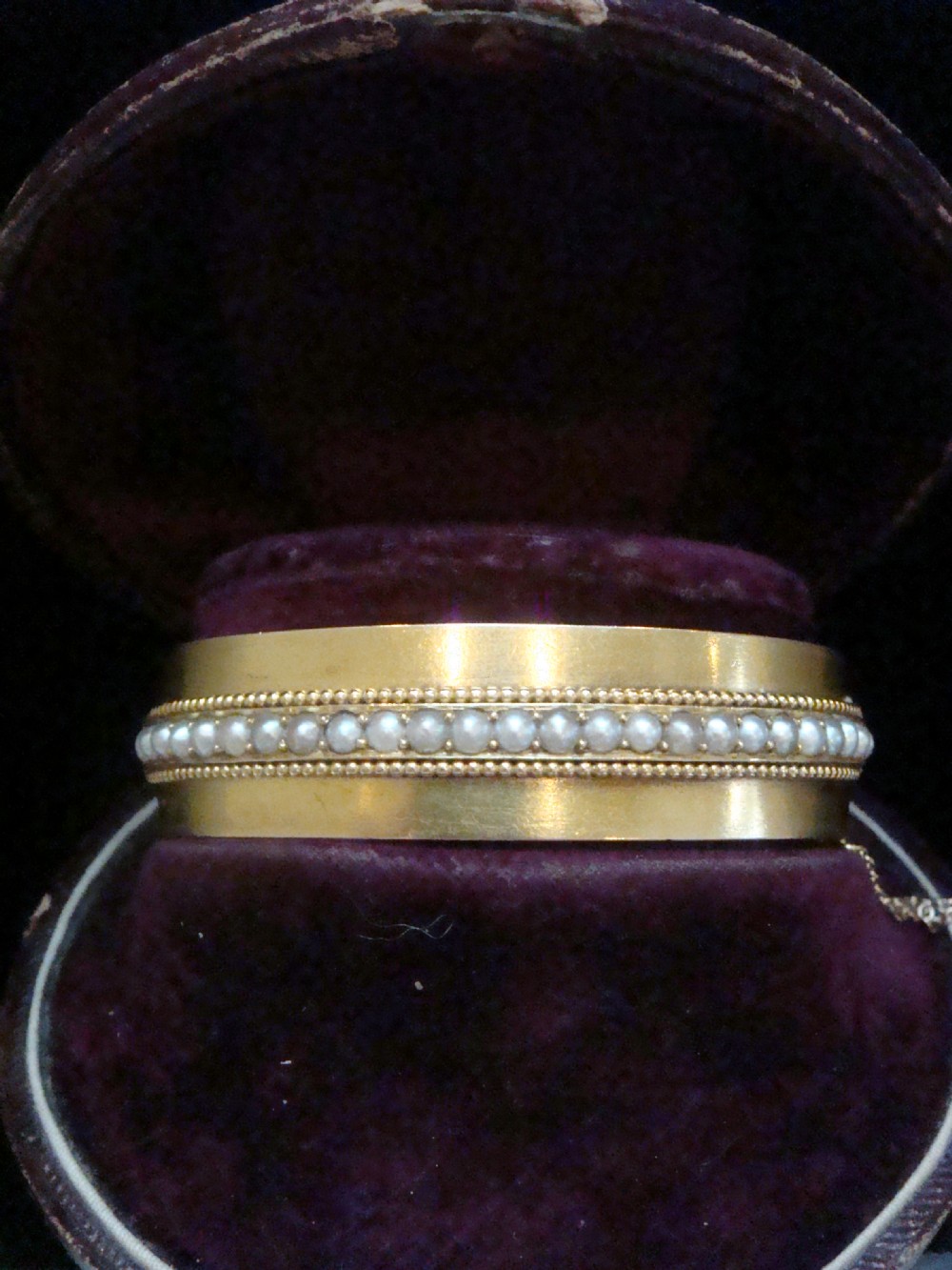 An antique 18ct gold cuff bracelet set with a central row of seed pearls framed by beaded borders, shown inside a velvet presentation box.