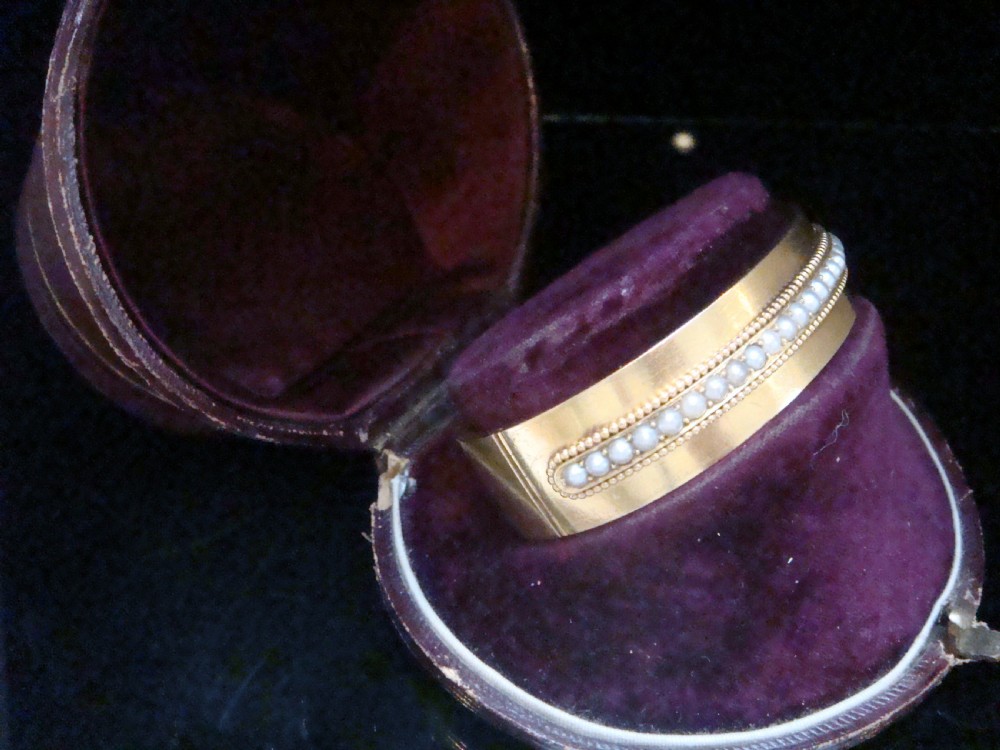 An antique 18ct gold cuff bracelet set with a central row of seed pearls framed by beaded borders, shown inside a velvet presentation box. View II