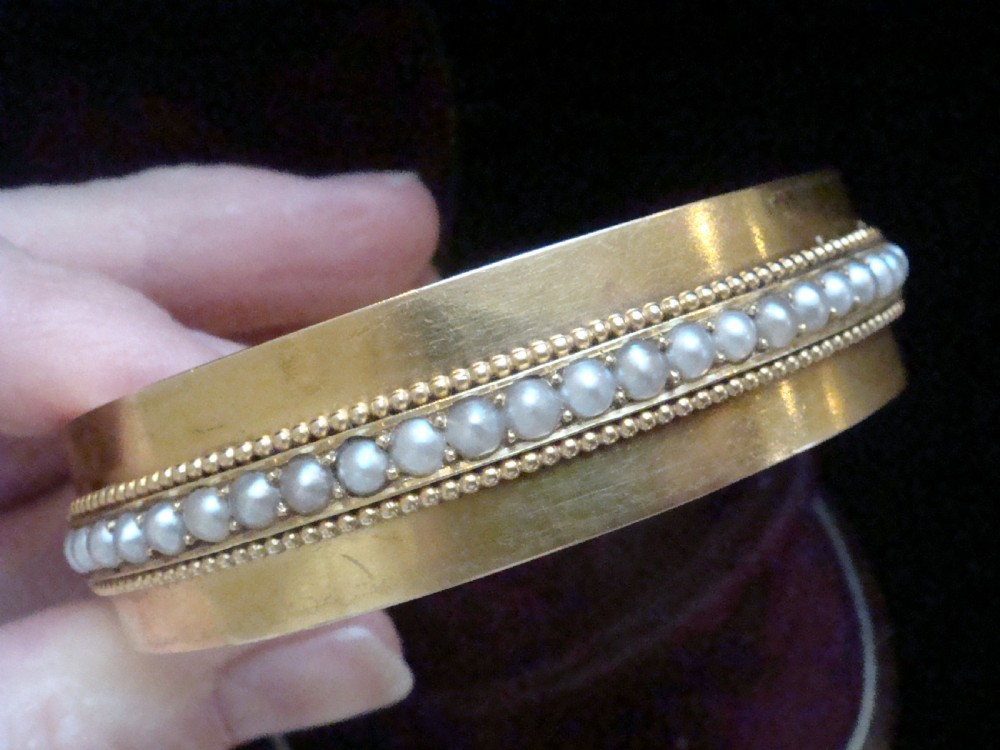 An antique 18ct gold cuff bracelet set with a central row of seed pearls framed by beaded borders, shown inside a velvet presentation box. View IV