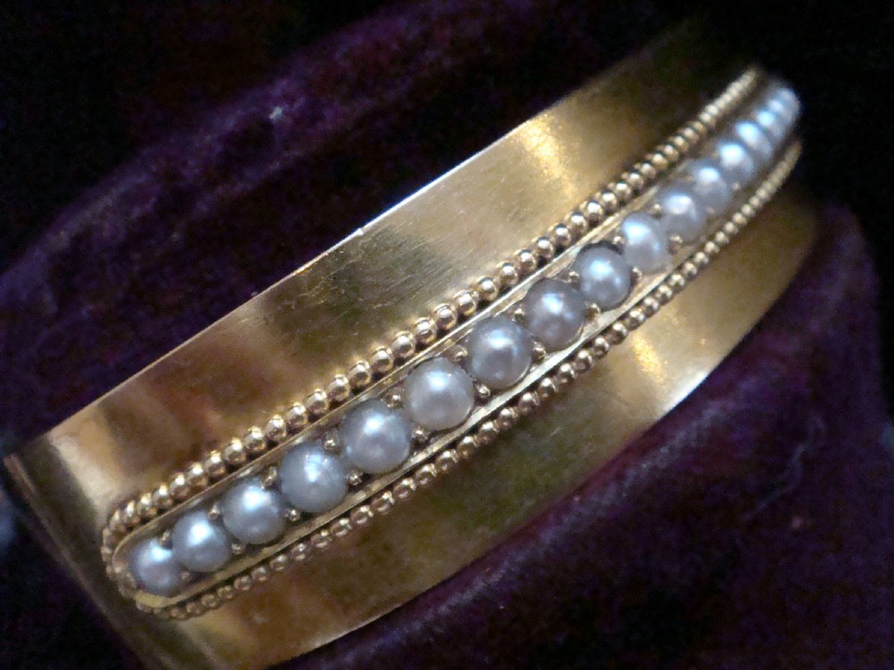 An antique 18ct gold cuff bracelet set with a central row of seed pearls framed by beaded borders, shown inside a velvet presentation box. View V