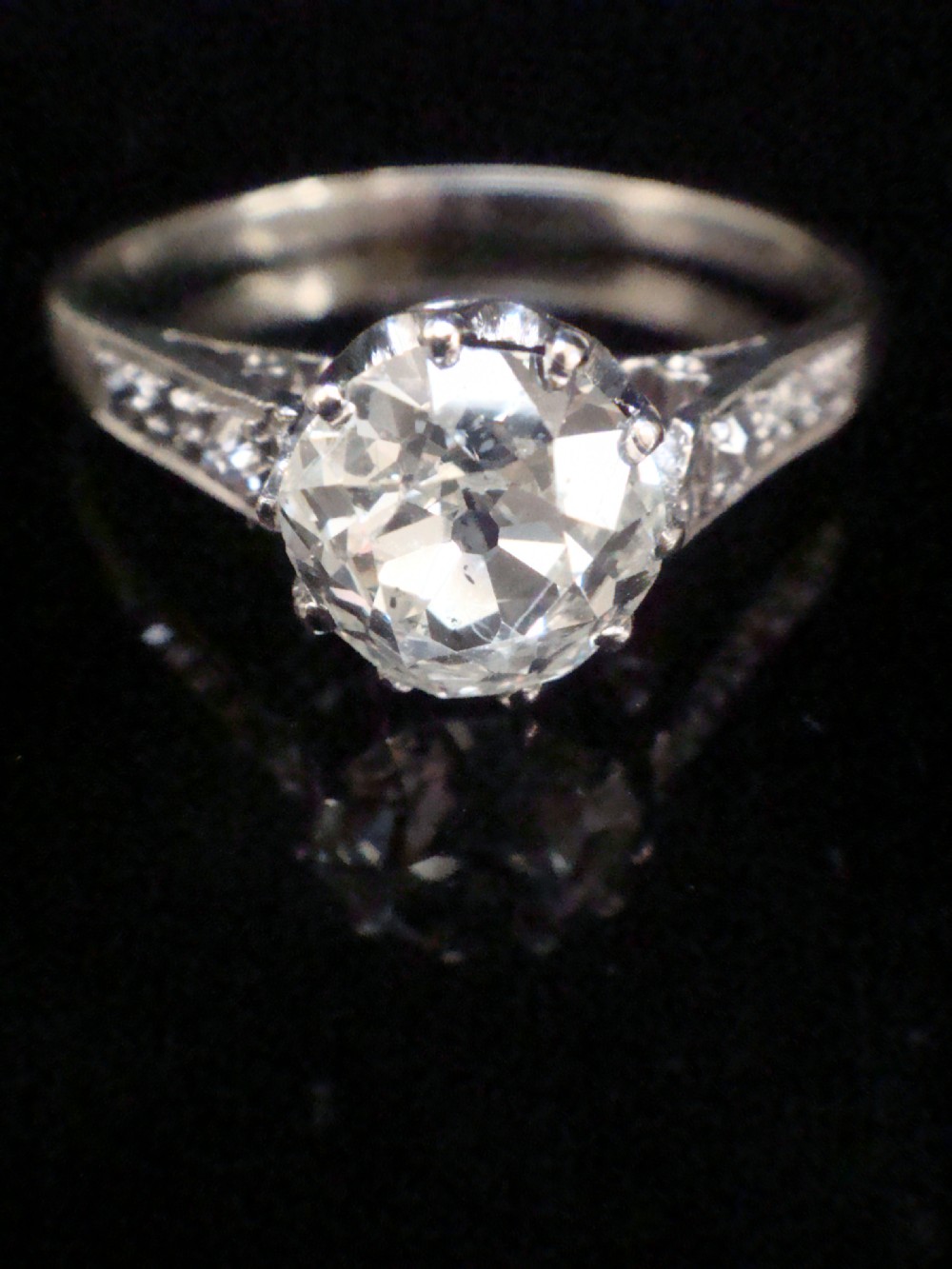 An Edwardian platinum solitaire ring featuring a round central diamond with small diamond accents set into the shoulders.