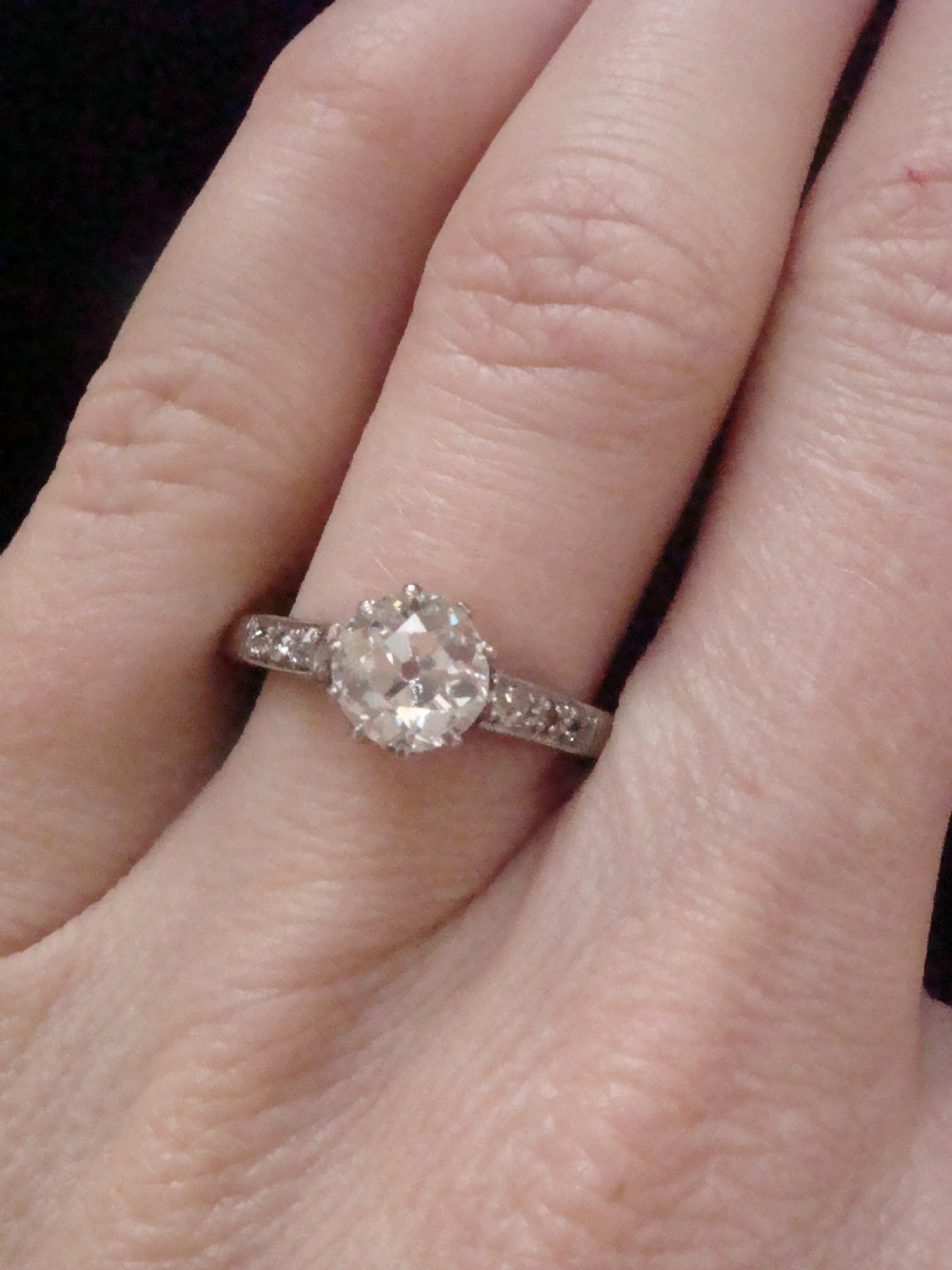 An Edwardian platinum solitaire ring featuring a round central diamond with small diamond accents set into the shoulders. View III
