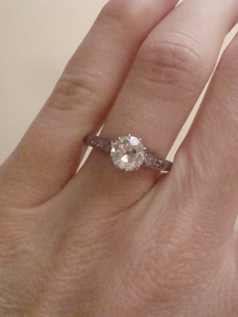 An Edwardian platinum solitaire ring featuring a round central diamond with small diamond accents set into the shoulders. View IV