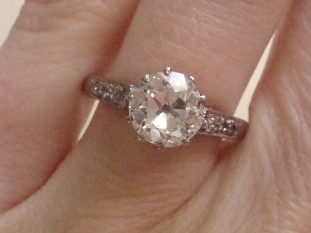 An Edwardian platinum solitaire ring featuring a round central diamond with small diamond accents set into the shoulders. View V
