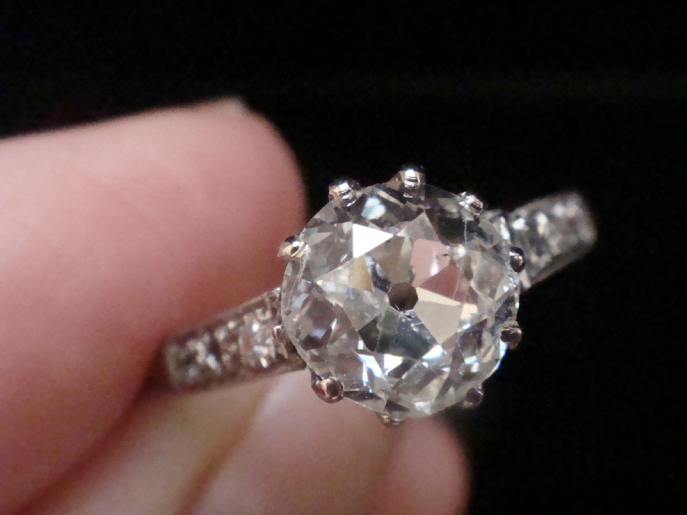 An Edwardian platinum solitaire ring featuring a round central diamond with small diamond accents set into the shoulders. View VI