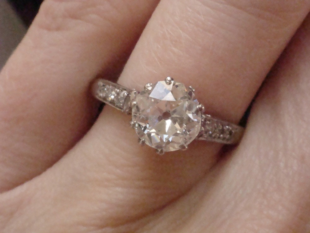 An Edwardian platinum solitaire ring featuring a round central diamond with small diamond accents set into the shoulders. View VII
