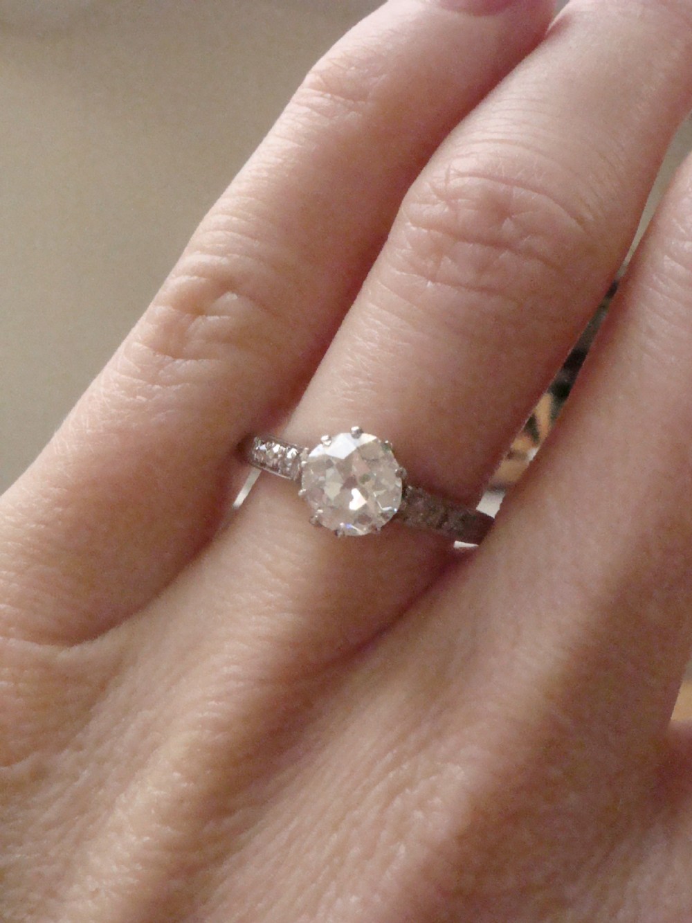 An Edwardian platinum solitaire ring featuring a round central diamond with small diamond accents set into the shoulders. View VIII