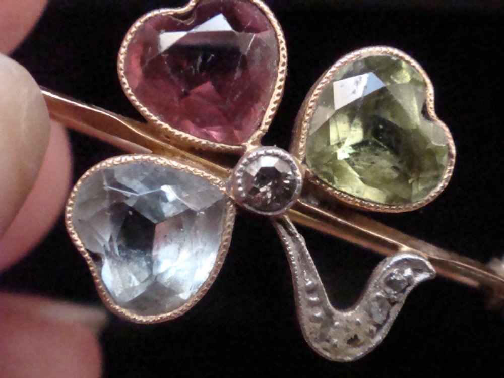 A Victorian 15ct yellow gold bar brooch featuring a central three-leaf clover crafted from heart-shaped tourmaline, aquamarine, and peridot, detailed with diamonds. View II