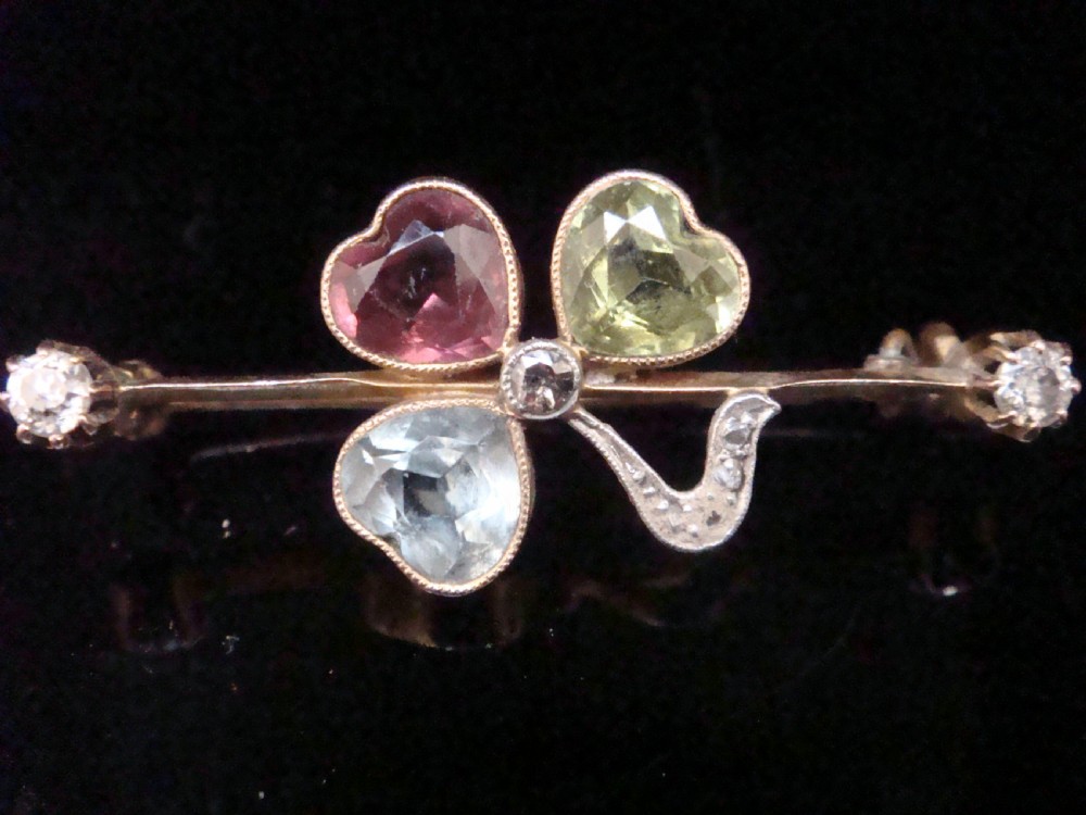 A Victorian 15ct yellow gold bar brooch featuring a central three-leaf clover crafted from heart-shaped tourmaline, aquamarine, and peridot, detailed with diamonds. View III