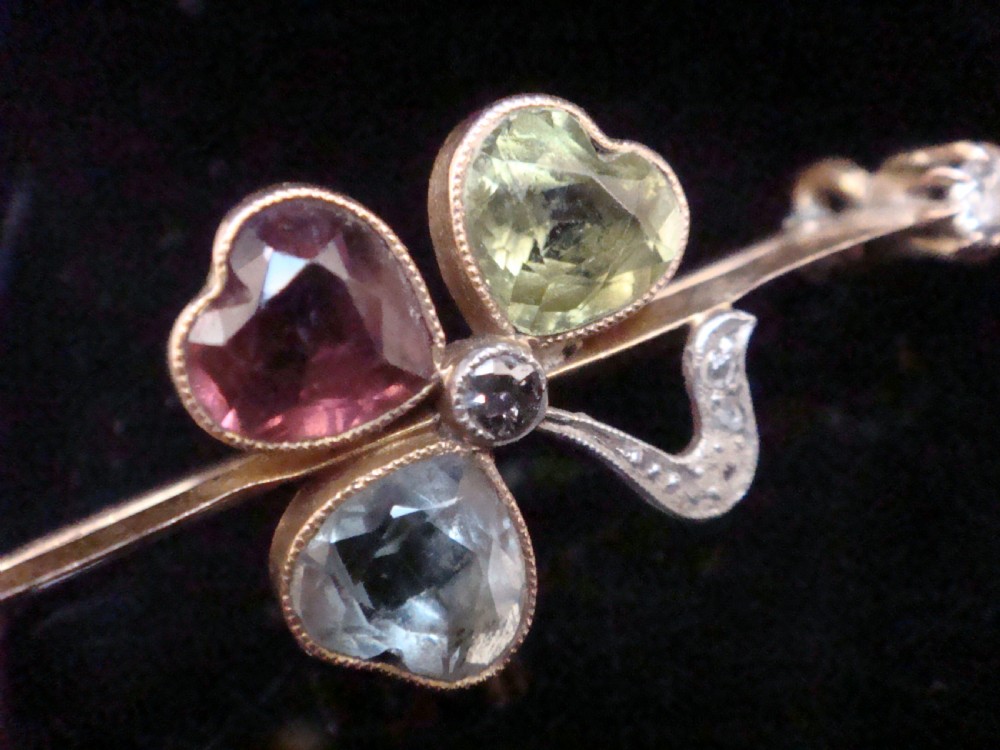 A Victorian 15ct yellow gold bar brooch featuring a central three-leaf clover crafted from heart-shaped tourmaline, aquamarine, and peridot, detailed with diamonds. View IV
