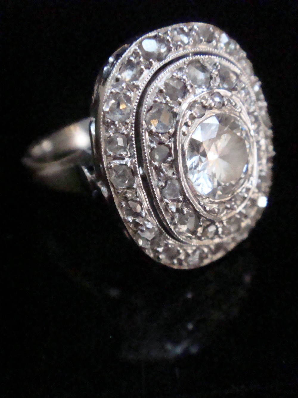An Edwardian 18ct white gold target cluster ring set with a central old cut diamond surrounded by concentric tiers of diamonds and fine millegrain details.
