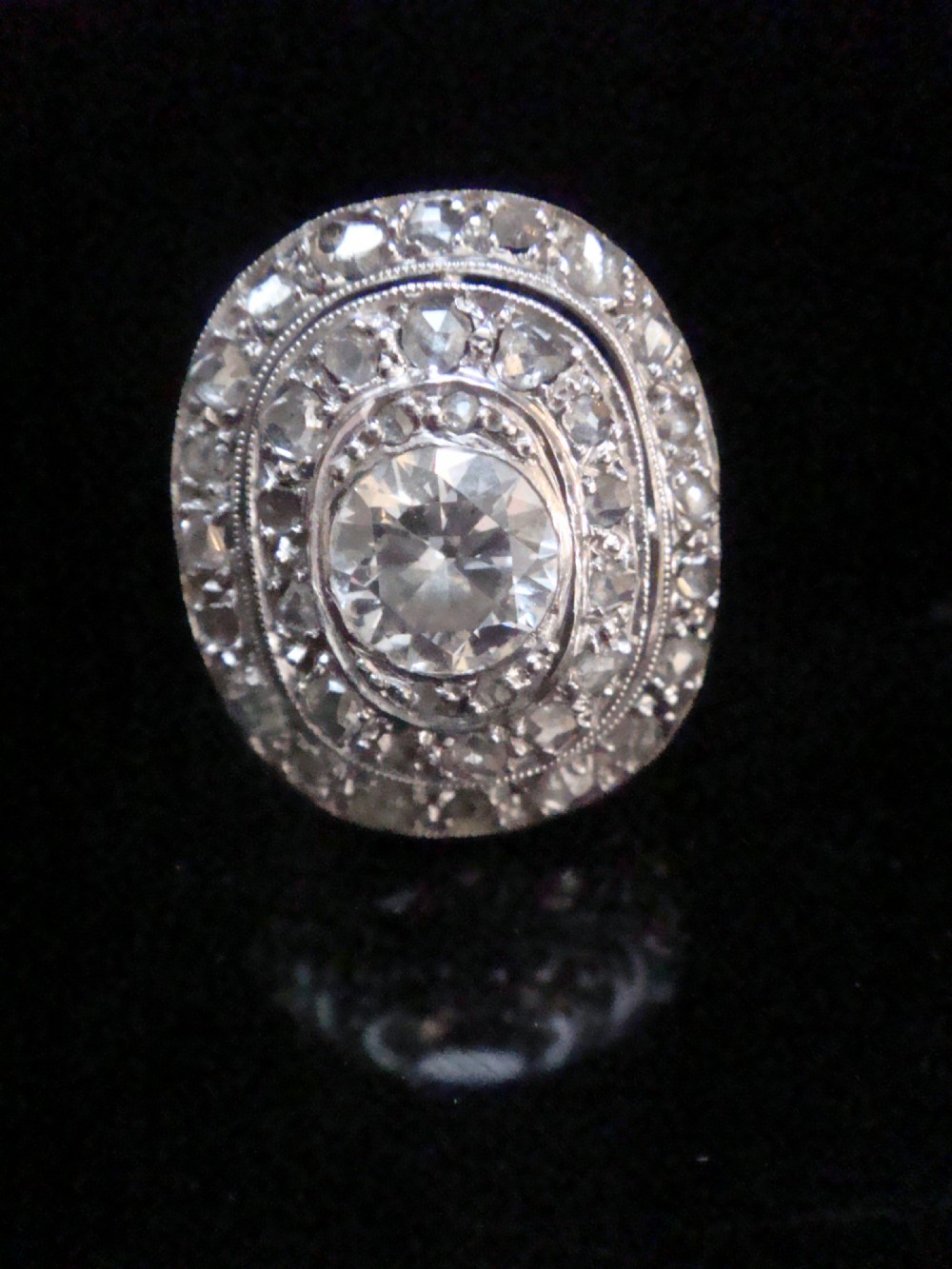 An Edwardian 18ct white gold target cluster ring set with a central old cut diamond surrounded by concentric tiers of diamonds and fine millegrain details. View IV
