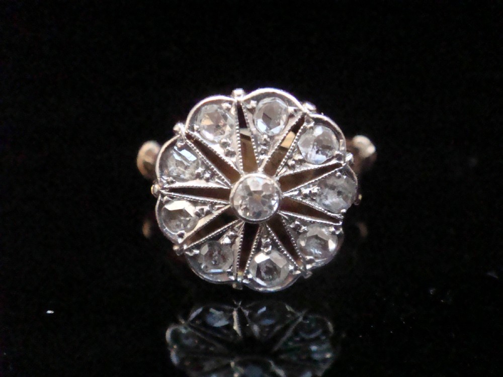 An Edwardian 18ct yellow gold and platinum ring featuring a floral starburst cluster set with old-cut diamonds.
