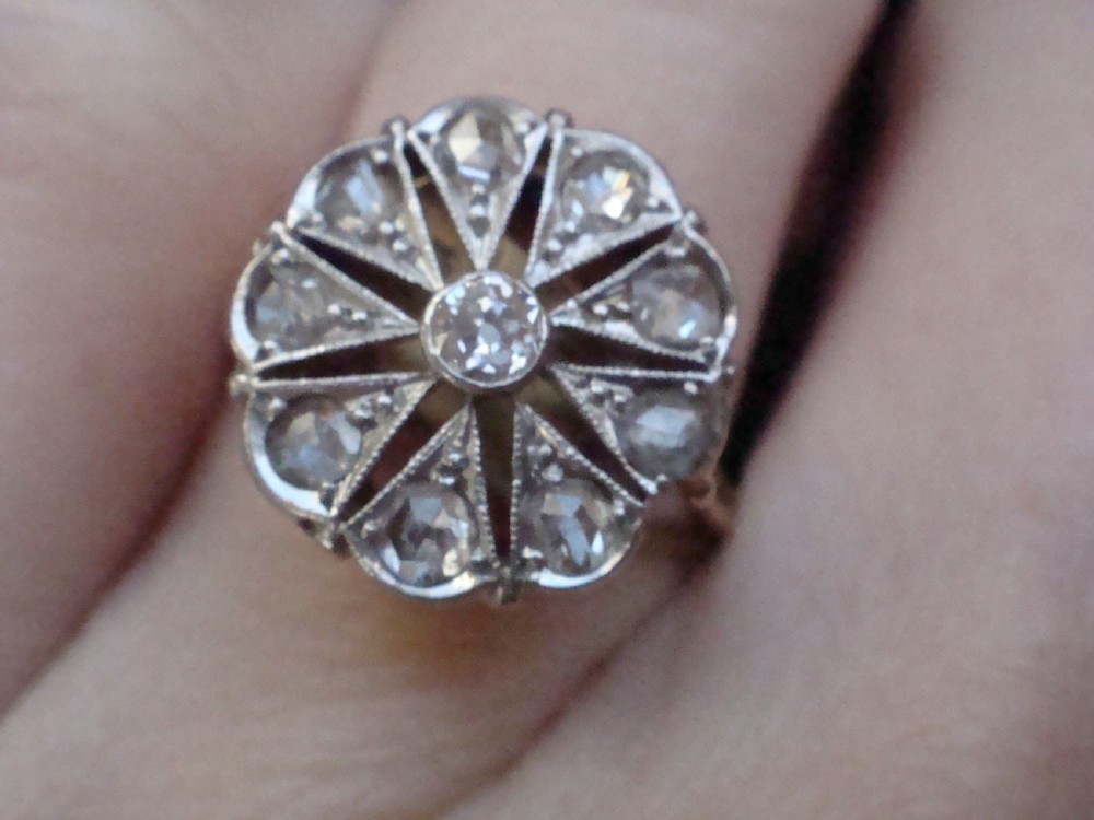 An Edwardian 18ct yellow gold and platinum ring featuring a floral starburst cluster set with old-cut diamonds. View V