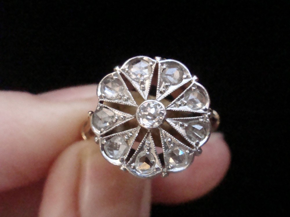 An Edwardian 18ct yellow gold and platinum ring featuring a floral starburst cluster set with old-cut diamonds. View VI