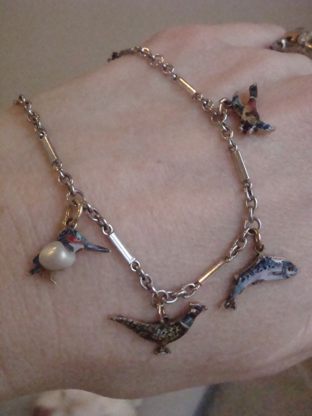An Edwardian gold link chain bracelet featuring polychrome enamelled wildlife charms including game birds and a fish. View X