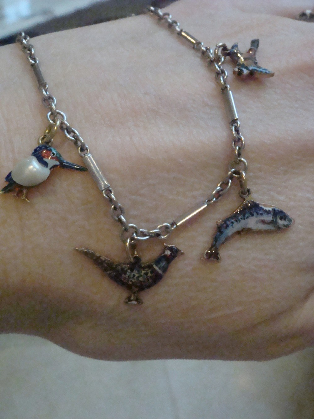 An Edwardian gold link chain bracelet featuring polychrome enamelled wildlife charms including game birds and a fish. View XV