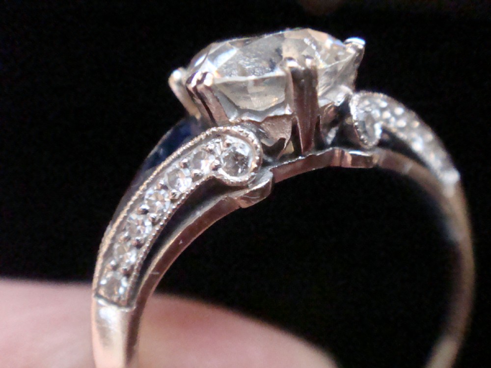 An Art Deco platinum solitaire ring featuring a large transitional-cut central diamond flanked by two triangular blue sapphires. View II