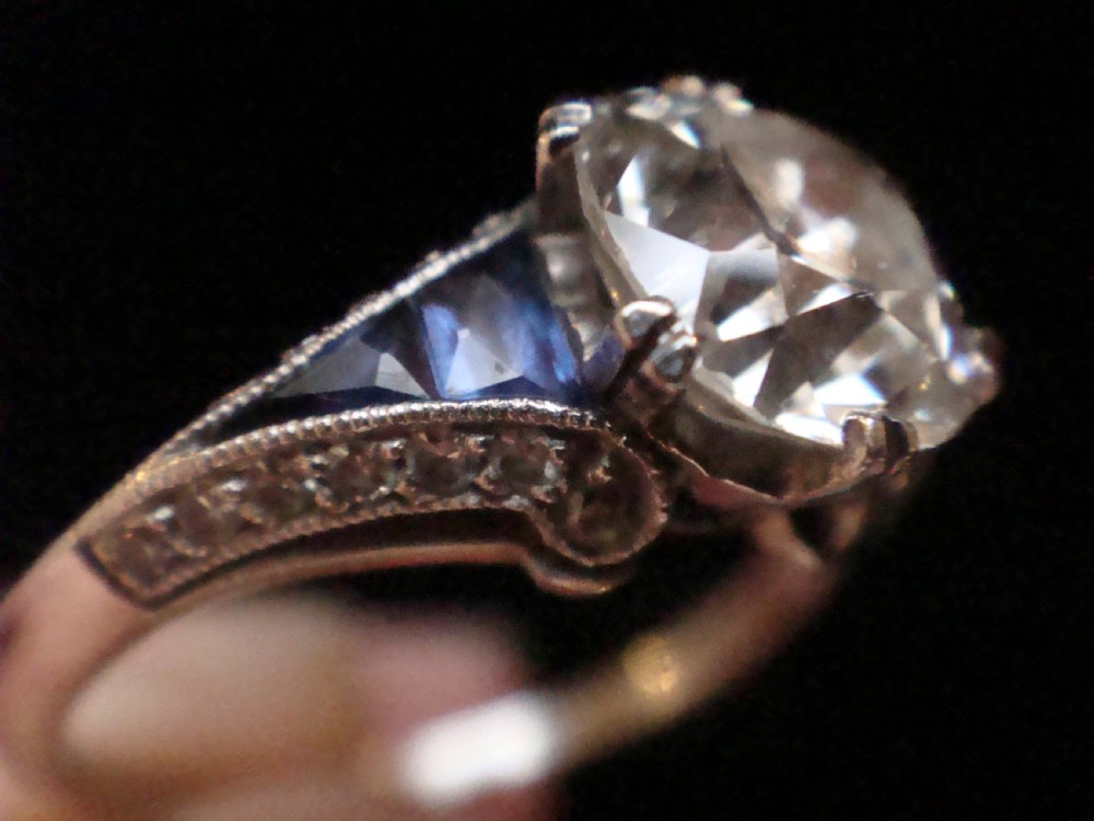 An Art Deco platinum solitaire ring featuring a large transitional-cut central diamond flanked by two triangular blue sapphires. View III