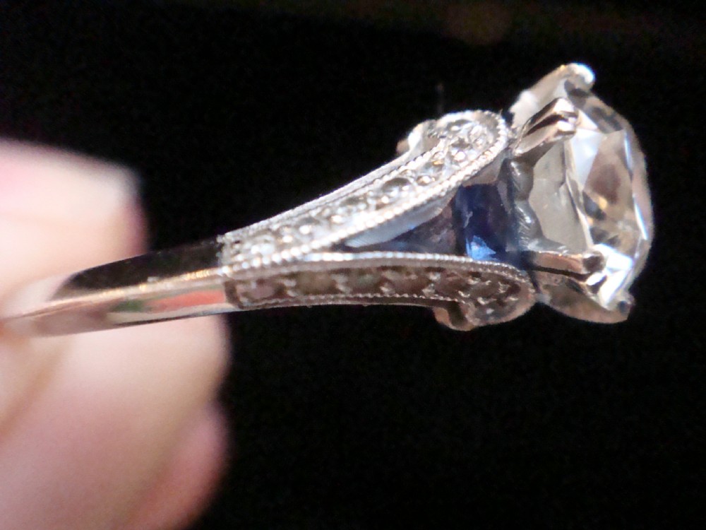An Art Deco platinum solitaire ring featuring a large transitional-cut central diamond flanked by two triangular blue sapphires. View V