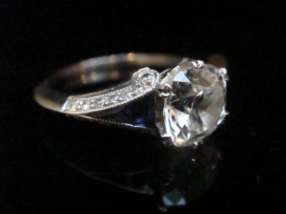 An Art Deco platinum solitaire ring featuring a large transitional-cut central diamond flanked by two triangular blue sapphires. View VI