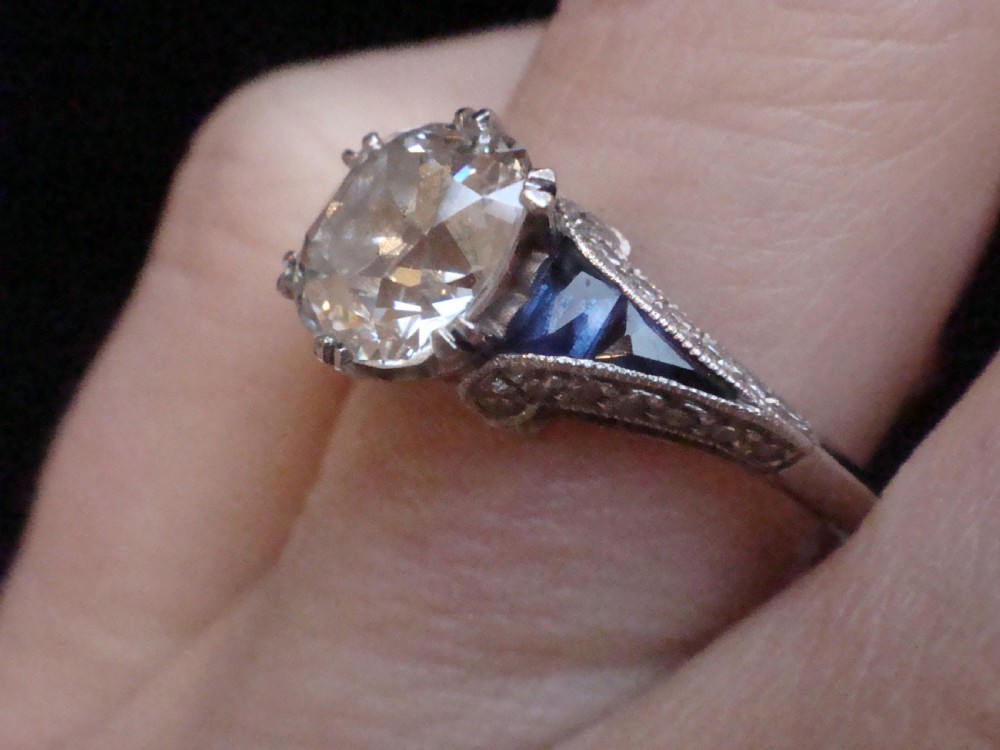 An Art Deco platinum solitaire ring featuring a large transitional-cut central diamond flanked by two triangular blue sapphires. View IX