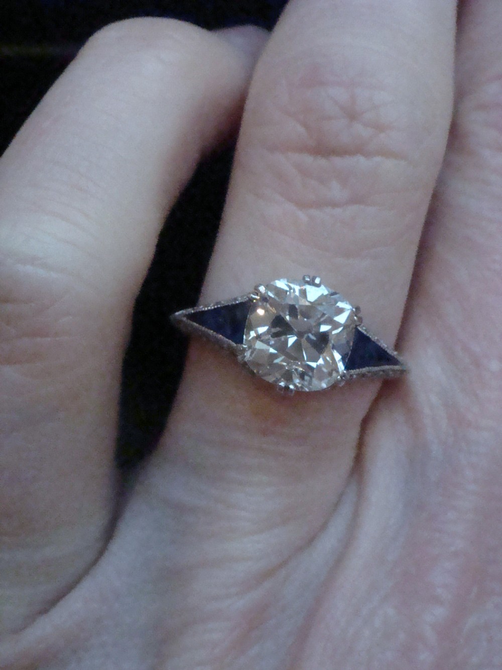 An Art Deco platinum solitaire ring featuring a large transitional-cut central diamond flanked by two triangular blue sapphires. View XV