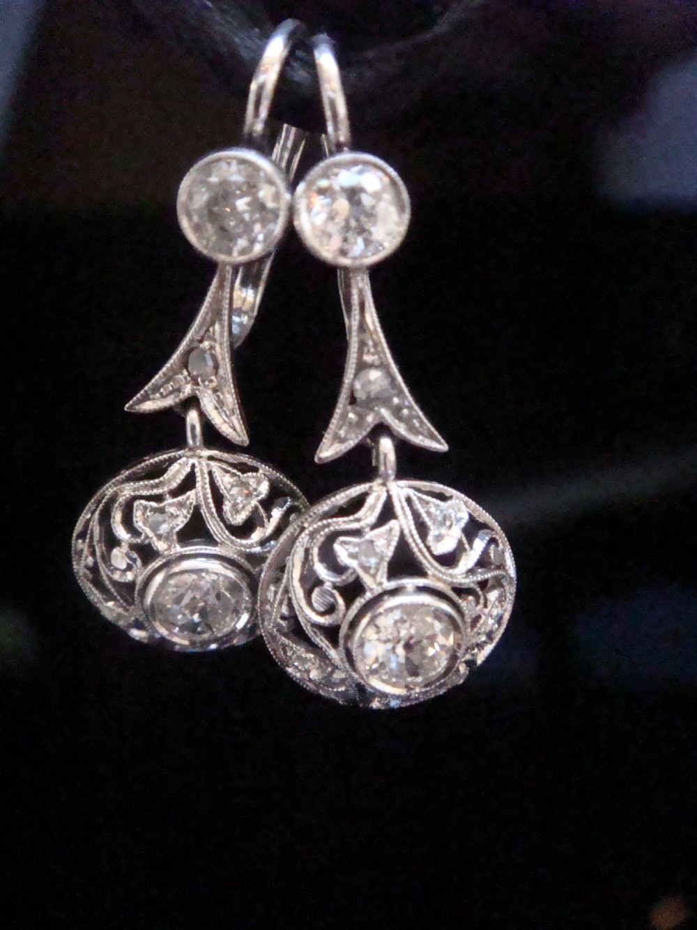 A pair of Edwardian 18ct white gold drop earrings featuring old cut diamonds set within circular openwork filigree mounts.