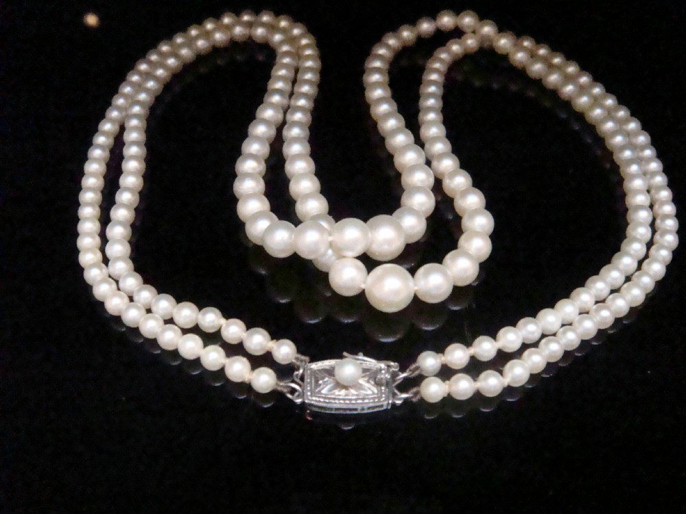A double strand graduated white cultured pearl necklace featuring an ornate silver box clasp set with a single pearl.
