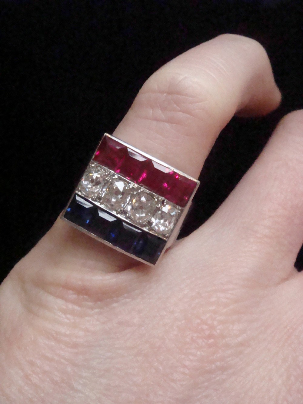 An Art Deco platinum rectangular plaque ring set with horizontal rows of red rubies, white diamonds, and blue sapphires. View III