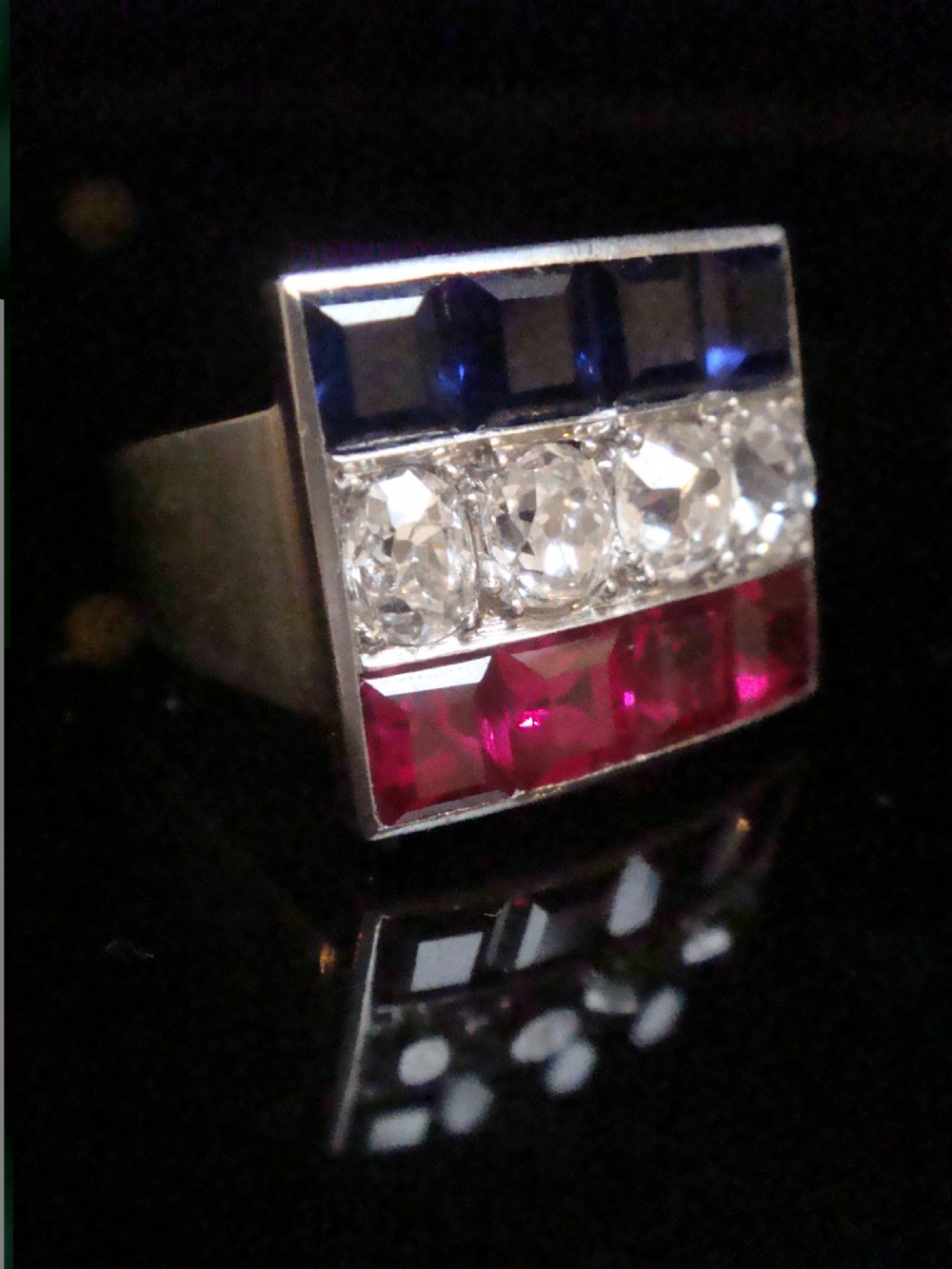 An Art Deco platinum rectangular plaque ring set with horizontal rows of red rubies, white diamonds, and blue sapphires. View IV