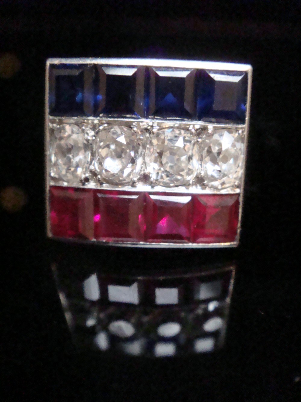 An Art Deco platinum rectangular plaque ring set with horizontal rows of red rubies, white diamonds, and blue sapphires. View V