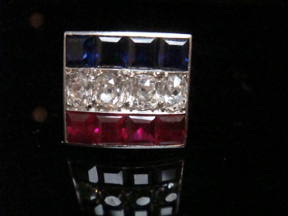 An Art Deco platinum rectangular plaque ring set with horizontal rows of red rubies, white diamonds, and blue sapphires. View IX