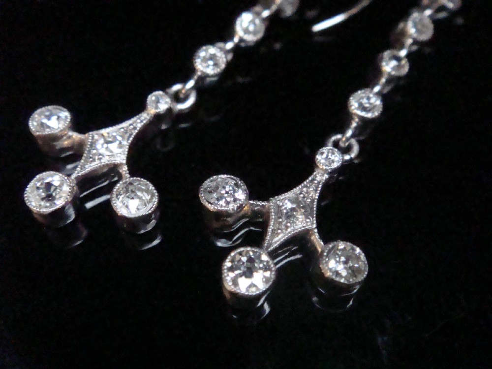 Pair of Edwardian platinum drop earrings featuring articulated lines of bezel-set round old cut diamonds terminating in geometric drops with hook fastenings. View II