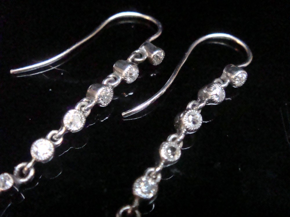 Pair of Edwardian platinum drop earrings featuring articulated lines of bezel-set round old cut diamonds terminating in geometric drops with hook fastenings. View IV