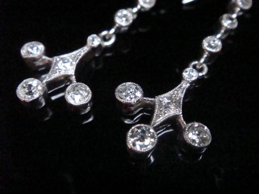 Pair of Edwardian platinum drop earrings featuring articulated lines of bezel-set round old cut diamonds terminating in geometric drops with hook fastenings. View V
