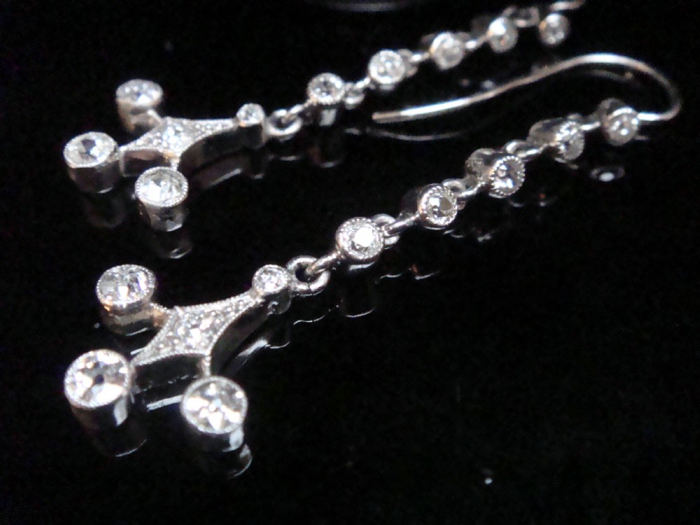 Pair of Edwardian platinum drop earrings featuring articulated lines of bezel-set round old cut diamonds terminating in geometric drops with hook fastenings. View VI