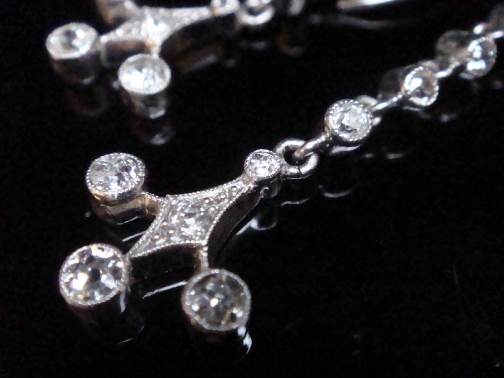 Pair of Edwardian platinum drop earrings featuring articulated lines of bezel-set round old cut diamonds terminating in geometric drops with hook fastenings. View VII