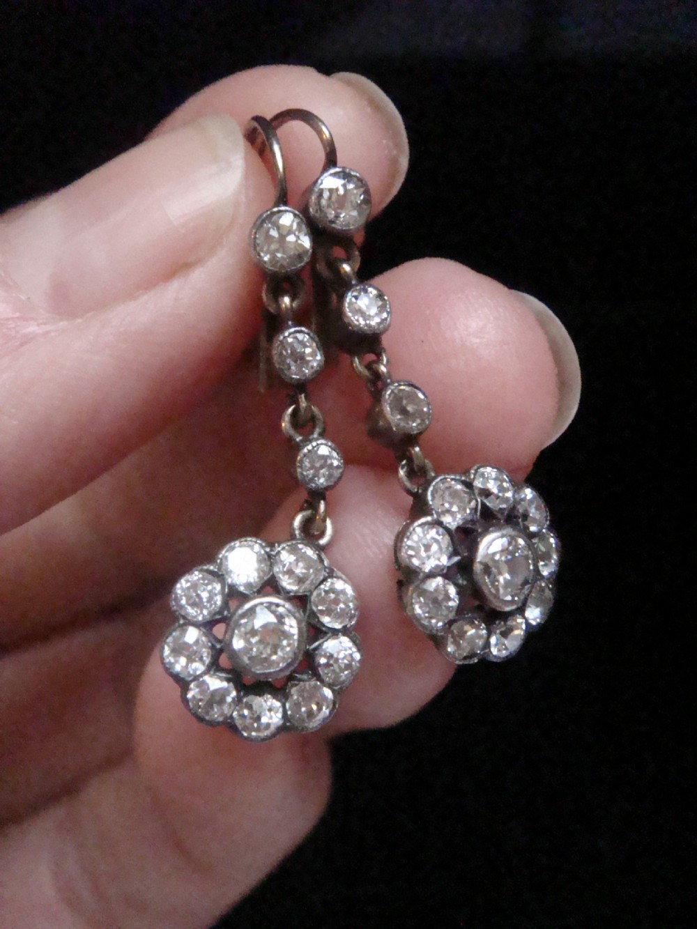 A pair of Edwardian silver and gold drop earrings featuring articulated strands of old cut diamonds leading to floral cluster drops.