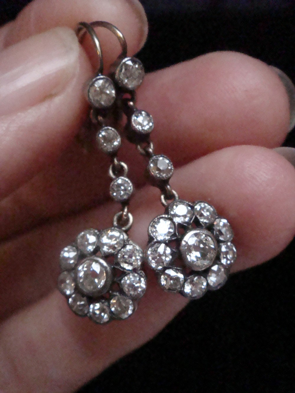 A pair of Edwardian silver and gold drop earrings featuring articulated strands of old cut diamonds leading to floral cluster drops. View V
