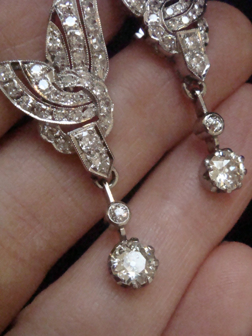 A pair of Art Deco 18ct white gold drop earrings stylised with geometric wing motifs set with diamonds and suspending articulated round old-cut diamond drops. View II