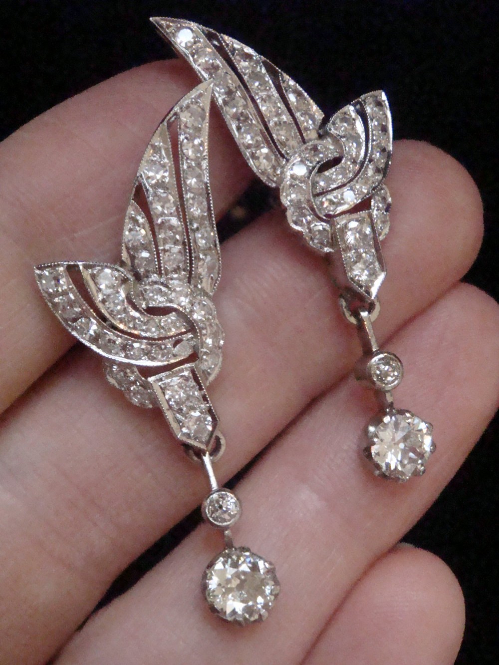A pair of Art Deco 18ct white gold drop earrings stylised with geometric wing motifs set with diamonds and suspending articulated round old-cut diamond drops. View III