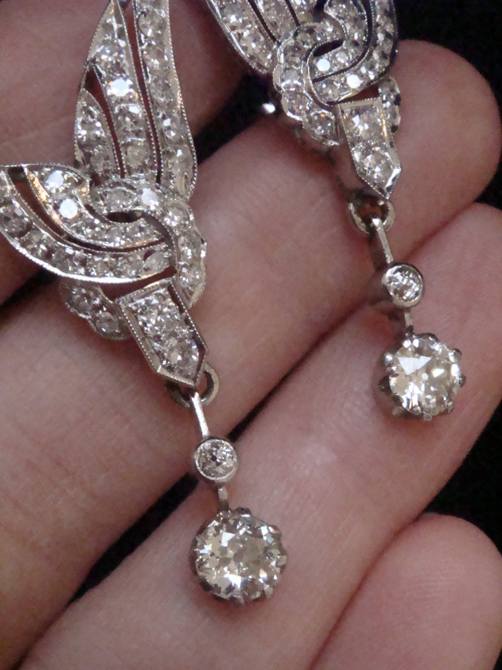 A pair of Art Deco 18ct white gold drop earrings stylised with geometric wing motifs set with diamonds and suspending articulated round old-cut diamond drops. View IV