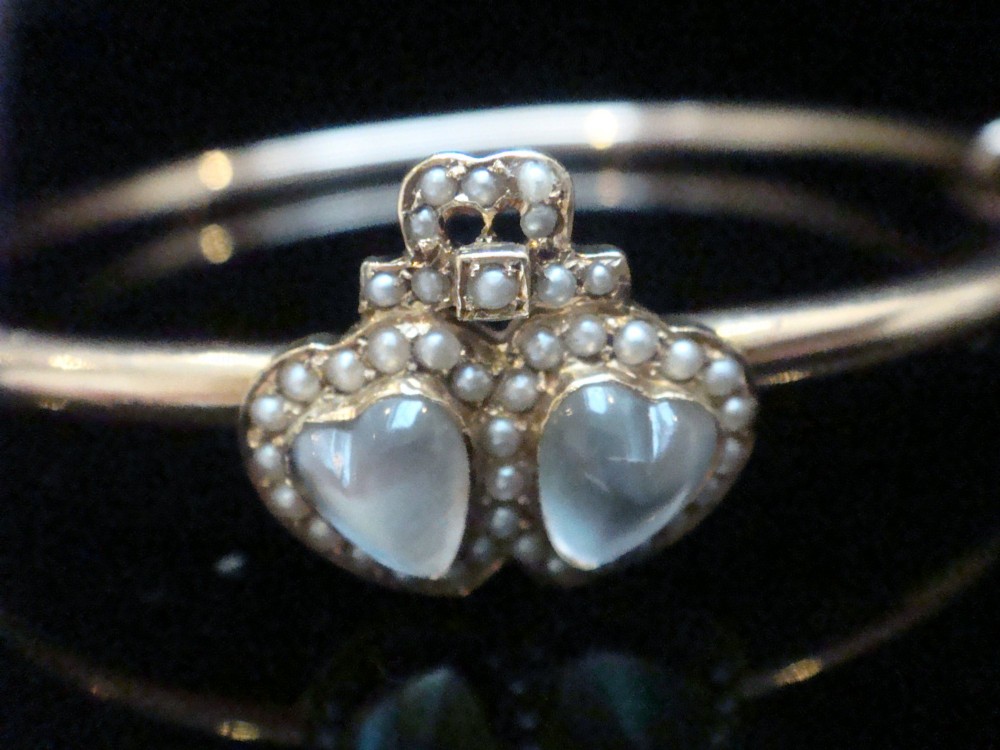 An antique 15ct gold hinged bangle featuring two heart-shaped cabochon moonstones framed by small seed pearls. View V